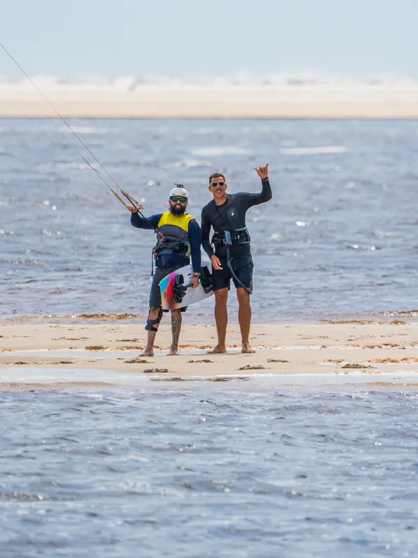 Duas pessoas num banco de areia no rio, com a barra e a prancha de kite