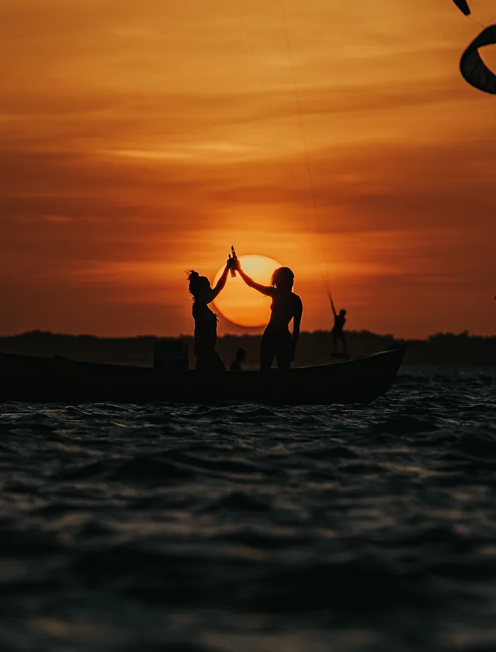 Duas pessoas brindando num barco ao pôr do sol